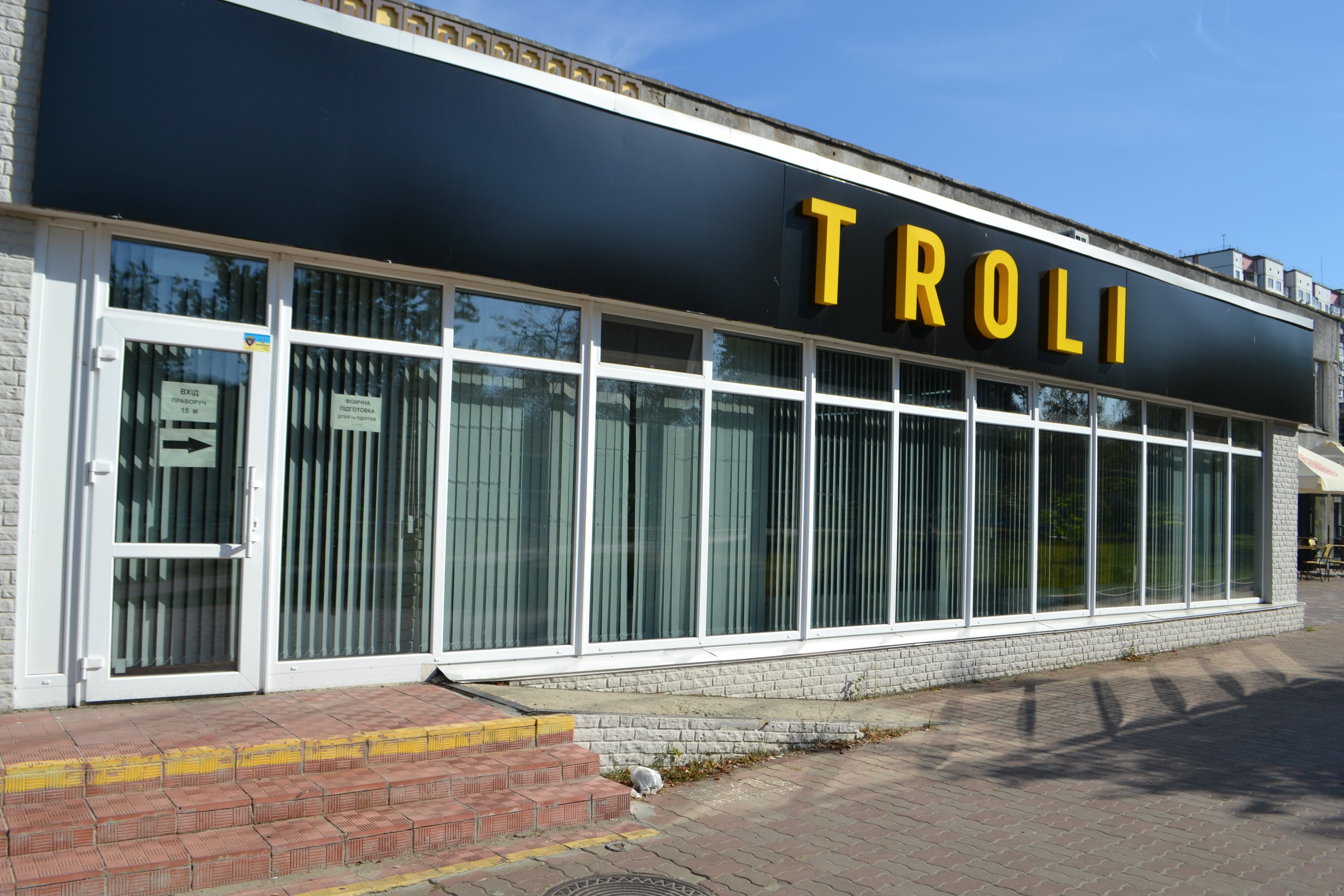 Спорт-клуб TROLLI – металопластикові панорамні вікна («в підлогу») білого кольору, великогабаритні прозорі склопакети. Велика реклама над входом спортклуба, пішохідна зона.